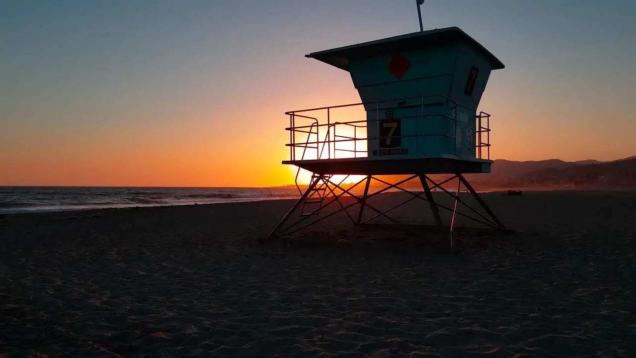 Slow crane shot rising up and revealing Lifeguard house  tower behind wooden log at sunset at San Buenaventura State Beach in Ventura California United States