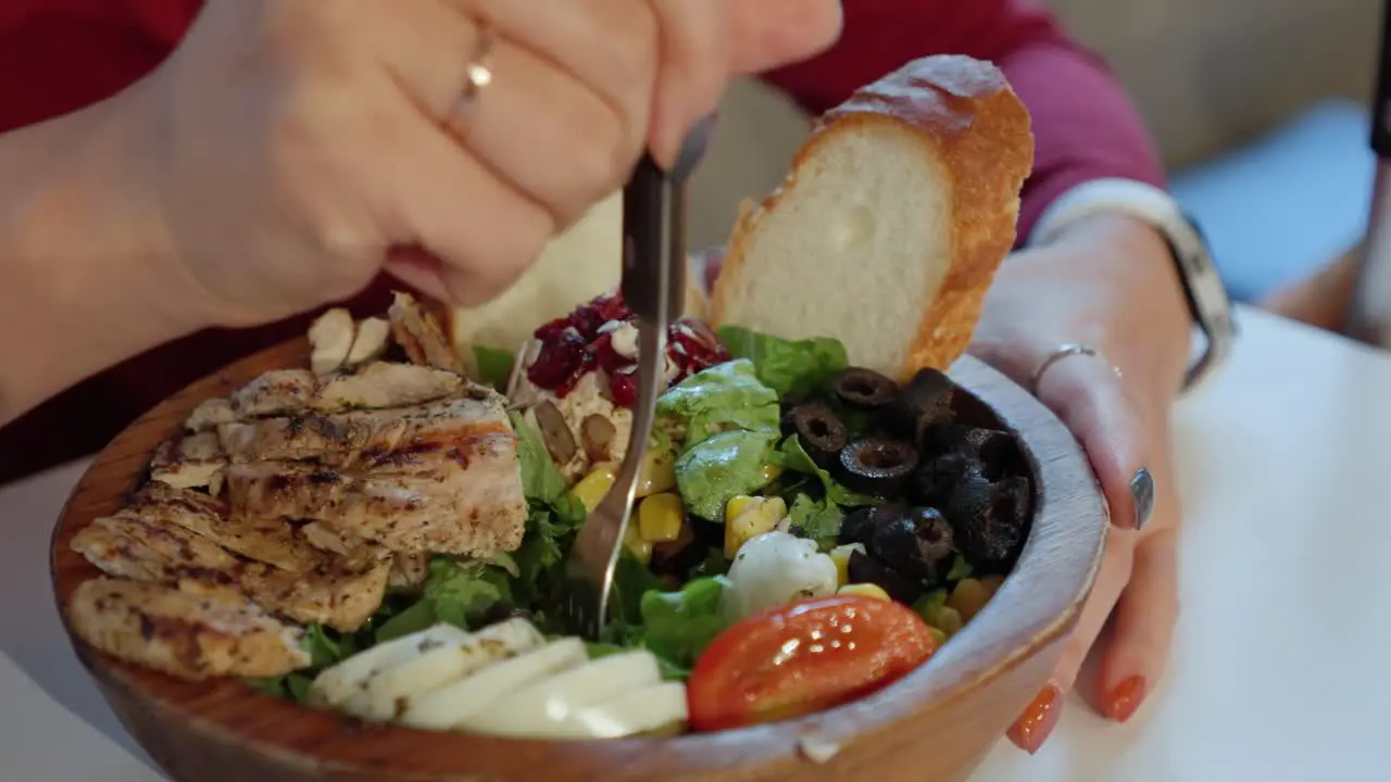 Woman begins eating fresh grilled chicken salad from wooden bowl