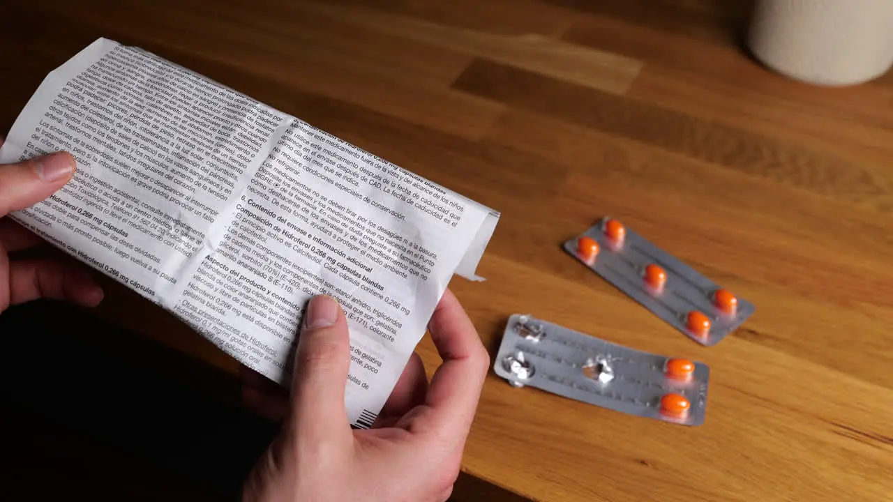 Hands holding medicine guide sheet with blister pack of orange medication tablets on wooden table