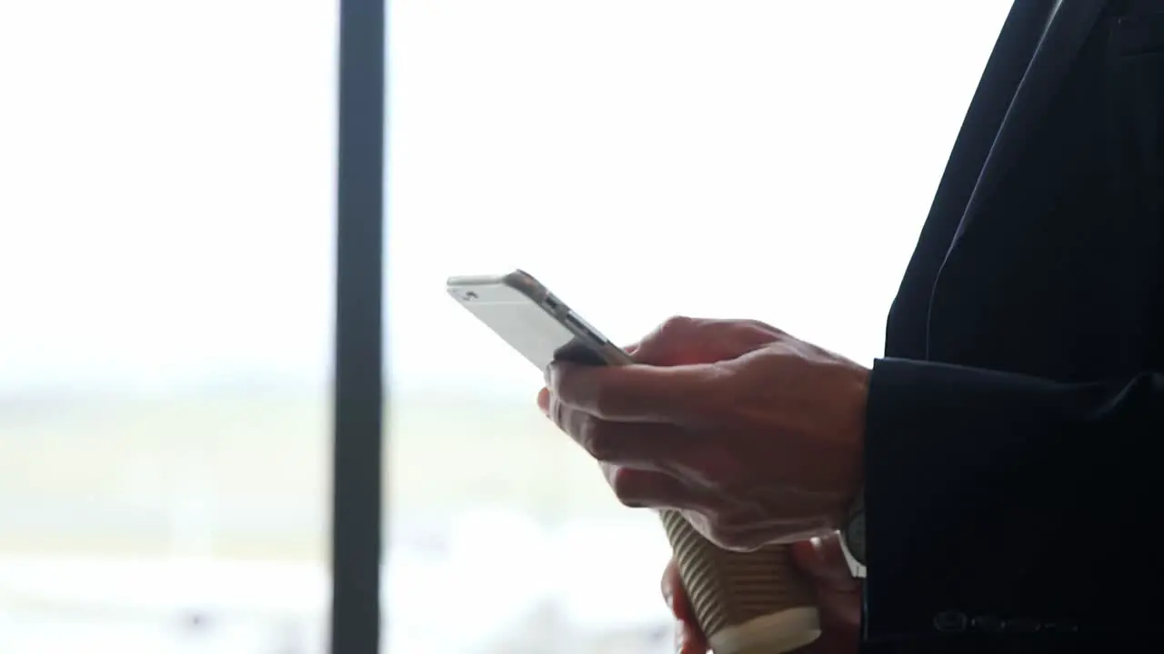 Businessman holding disposable cup texting on mobile phone 