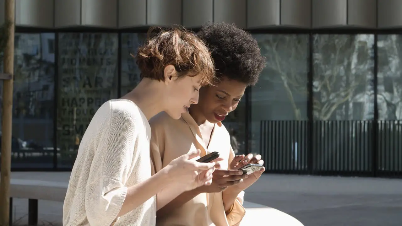 Side view of cheerful friends browsing internet via smartphones