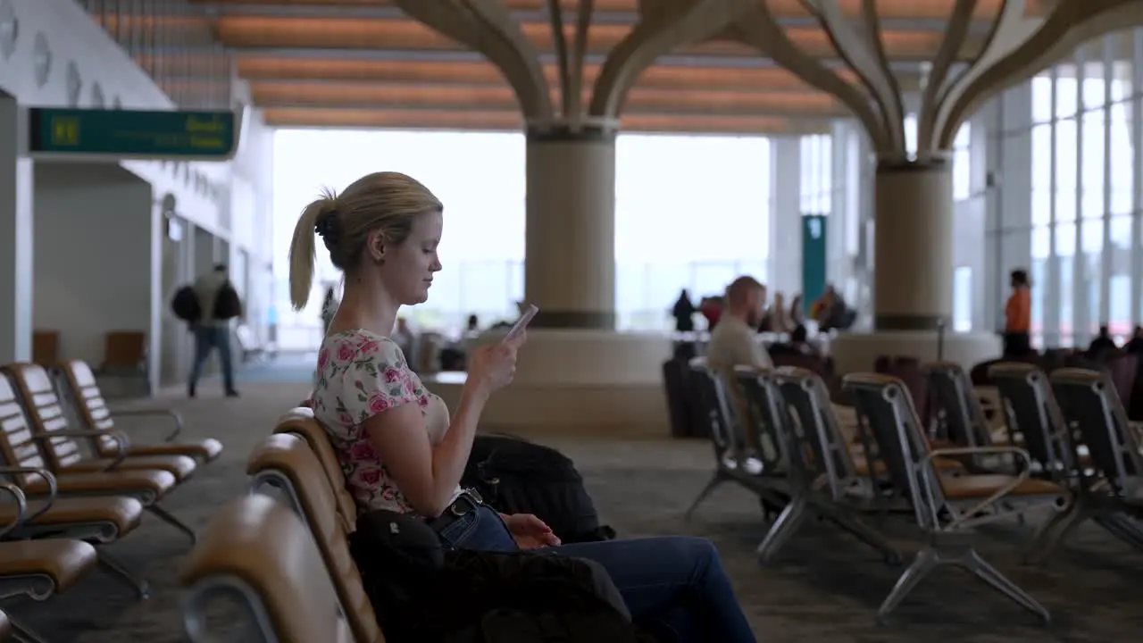 A young lady is sitting in the airport lounge and looks on her cell phone