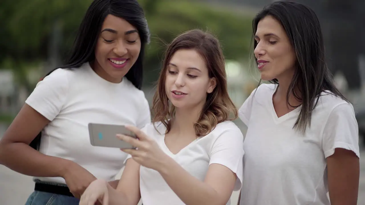 Three smiling women standing on street and looking at phone