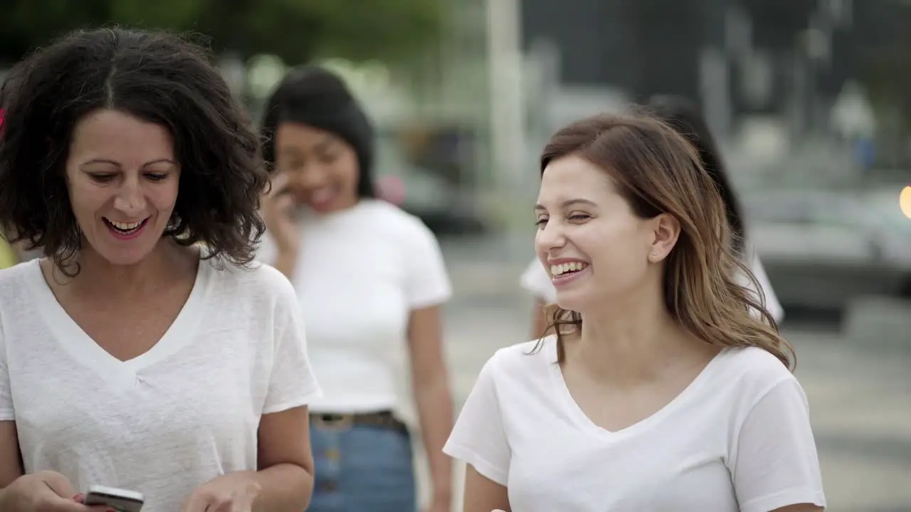 Cheerful friends walking on street with phones and talking