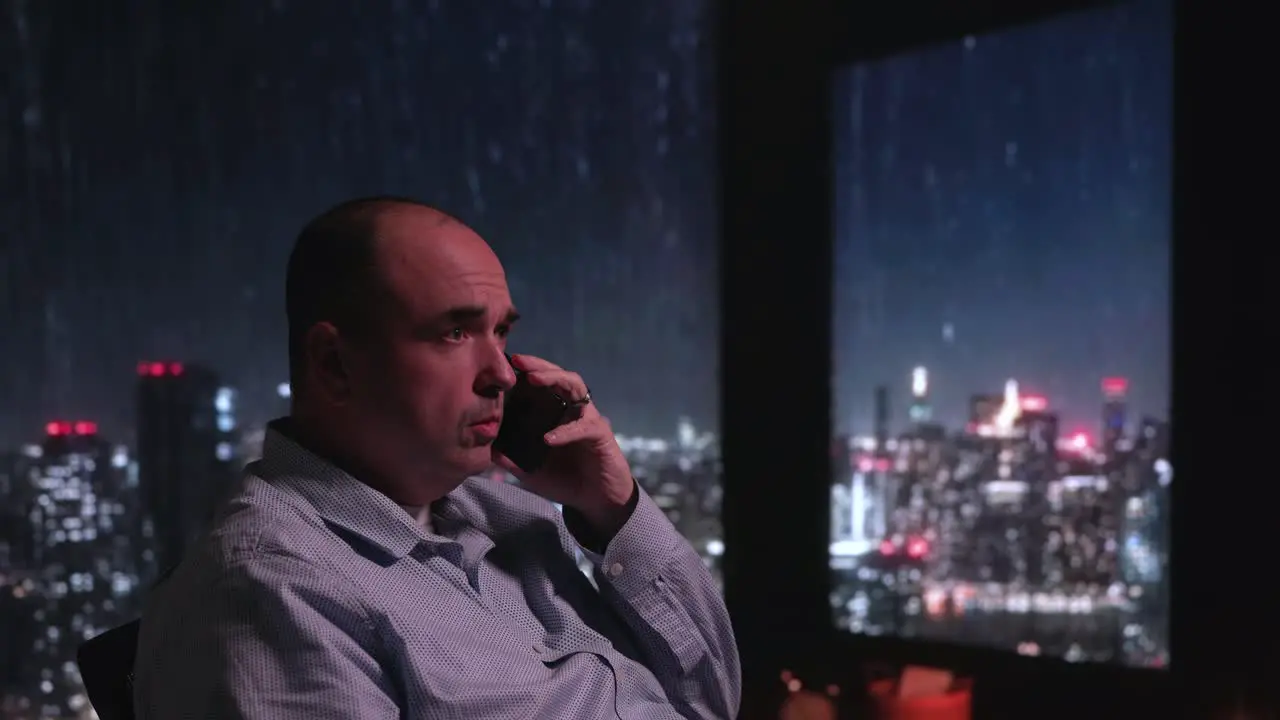 Man sitting near raining window on phone with city