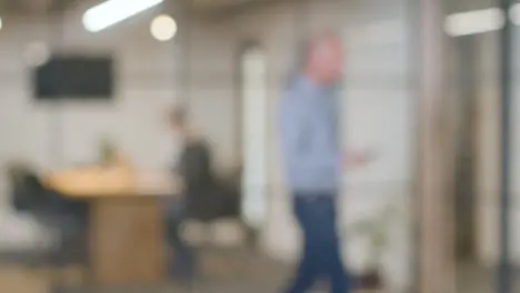 Defocused Background Shot Of Businesspeople Working At Desk In Office And Talking On Phone