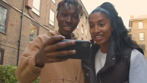 Close Up Of Young Couple Watching Sport On Mobile Phone In Urban City Area 