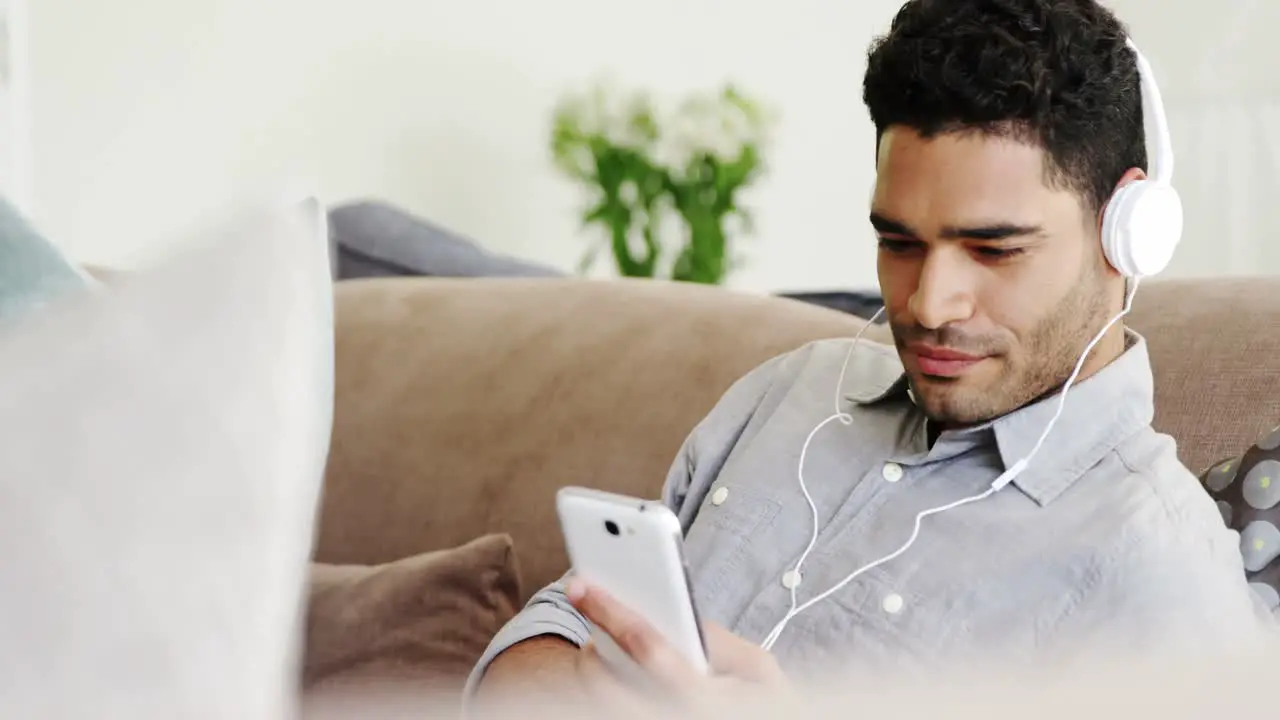 Happy man listening music on mobile phone in living room