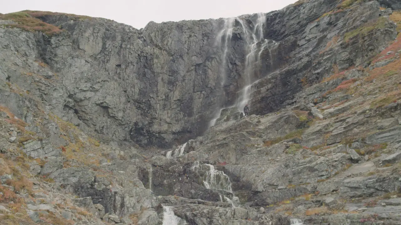 Person walks towards waterfall in rugged environment