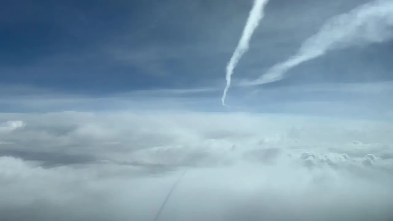 Sky view from a jet cockpit during flight overflying clouds and bellow another jet wake