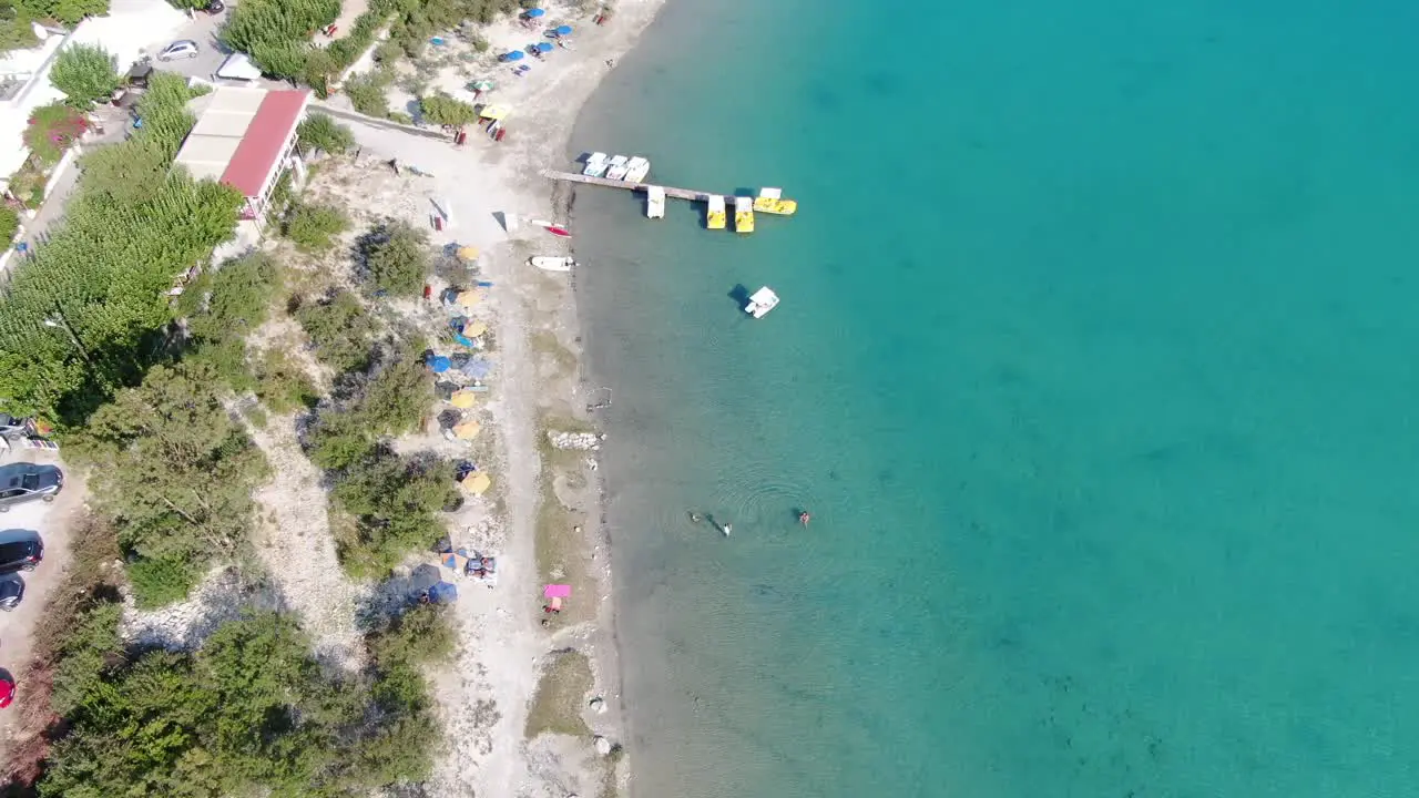 Drone view in Greece flying over a light and dark blue lake with small boats and surrounded by green landscape on a sunny day in Crete