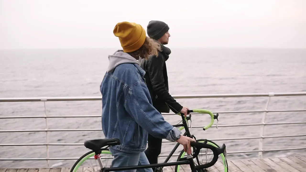 Beautiful Smiling Couple Of Young Hipsters Walking Together With Their Bikes Near The Sea At Autumn Day