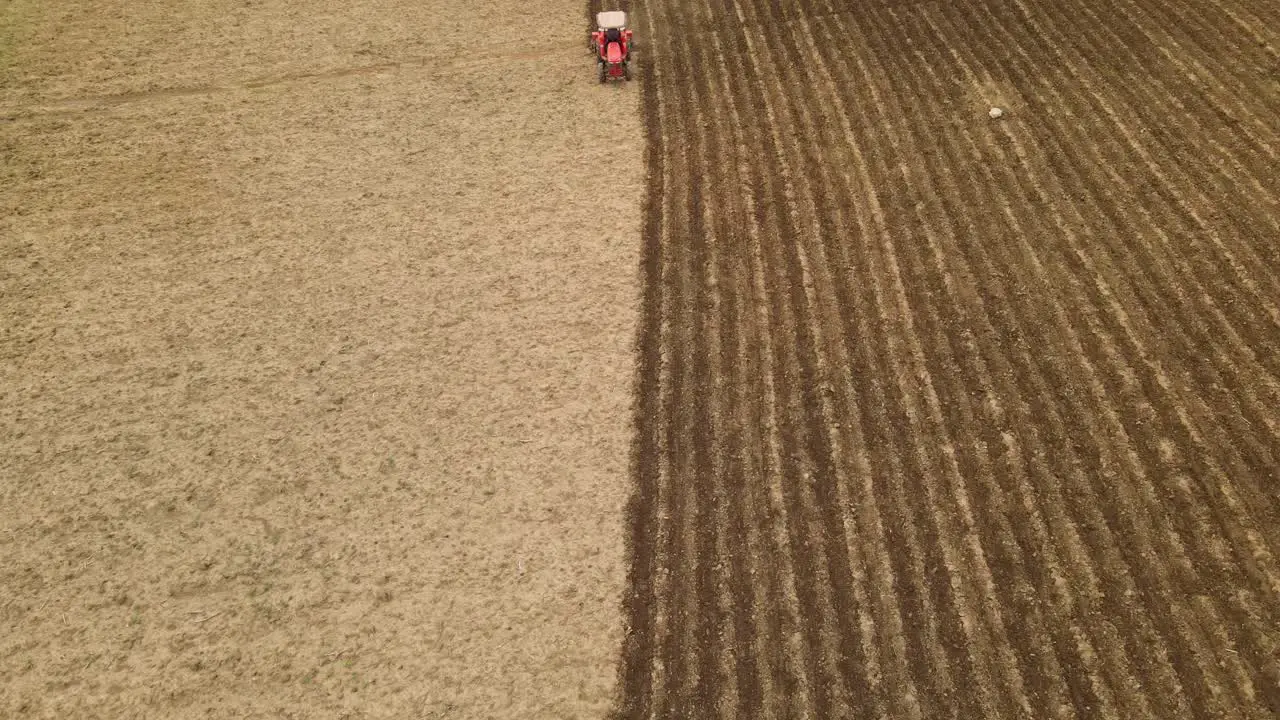 4K Static aerial shot of a red tractor tilling on a vertical line in the center of dusty farmland toward the camera showing a stark contrast on the land in agriculture industry Southeast Asia