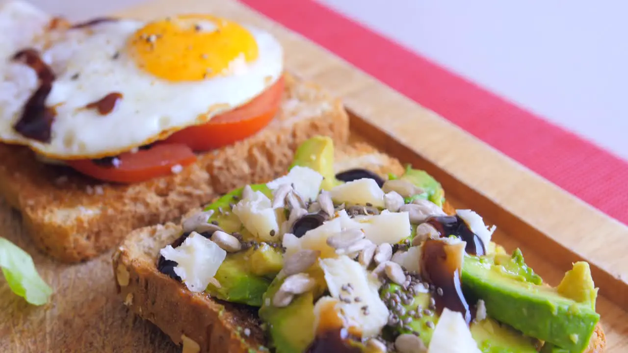 Nice close up of homemade fried egg on a toast with sliced tomatoes and avocado toast on wooden cutting board