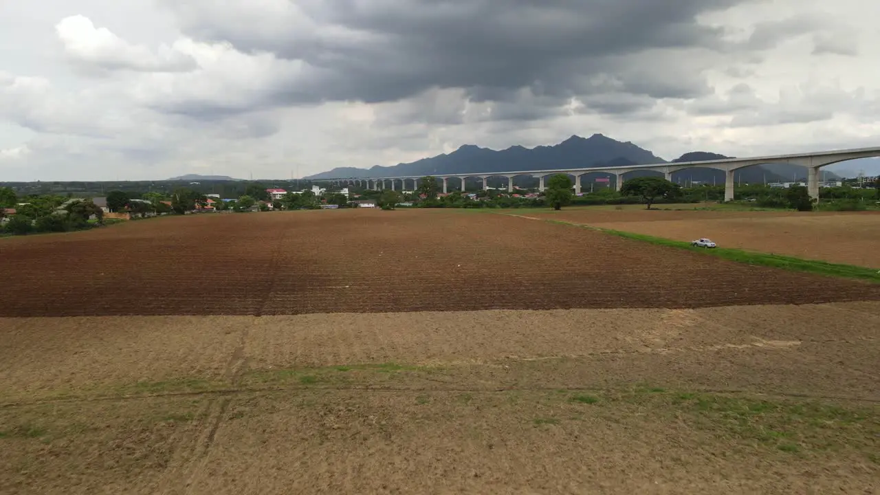 4K Aerial dolly out shot capturing the large piece of newly tilled agriculture farmland with Muak Lek mountains in the background and high-speed train line across the frame