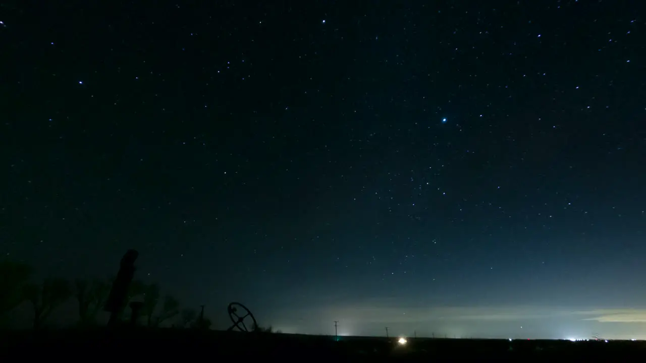 The silhouette of rusted tractor marks the horizon as the heavenly stars cross the night sky time lapse