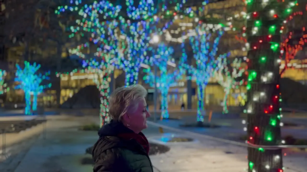 Senior woman walking in a city at night decorated with Christmas lights