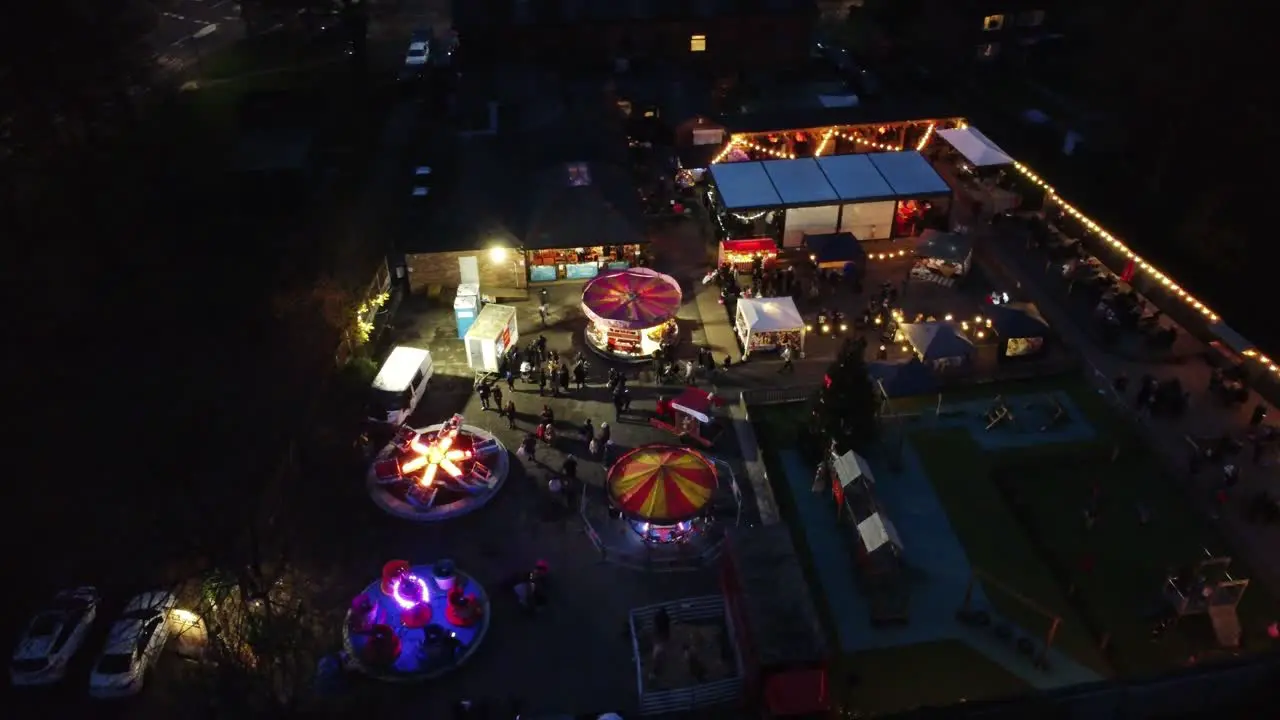 Illuminated Christmas fairground festival in neighbourhood car park at night aerial orbit view