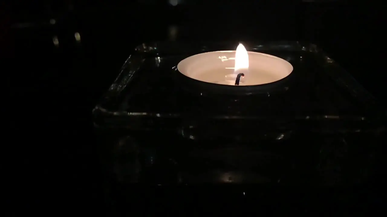 Romantic slow motion of tea candle on glass table at night with glow and reflection