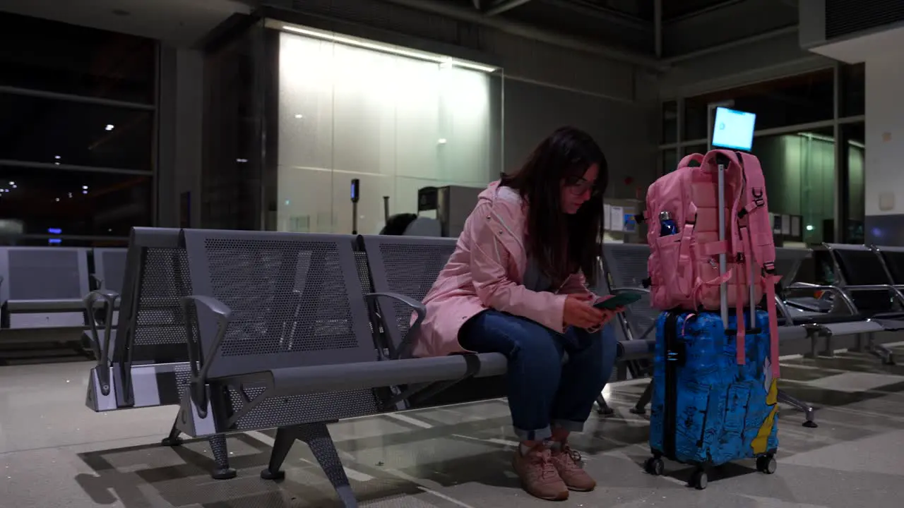 Woman waits her flight next to luggage playing with phone while coughs