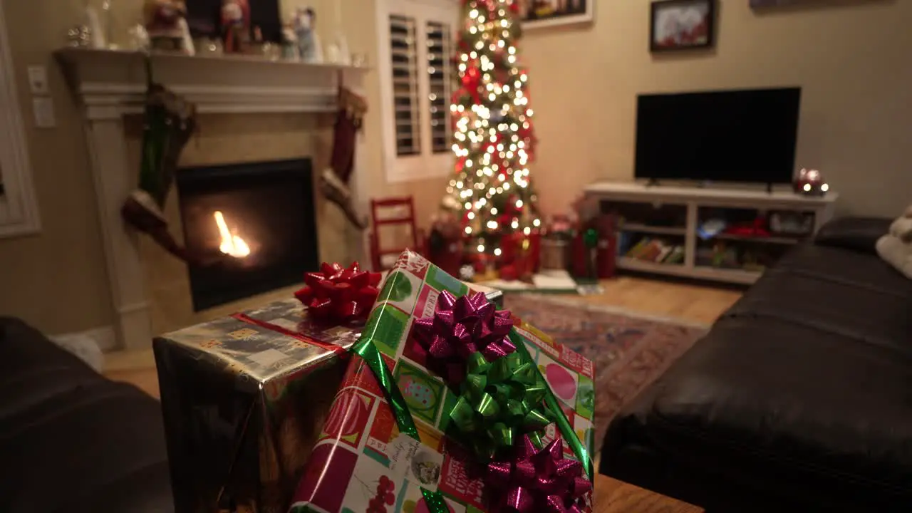 Christmas gifts with the Christmas tree in the background with a cozy fireplace sliding tilt up reveal