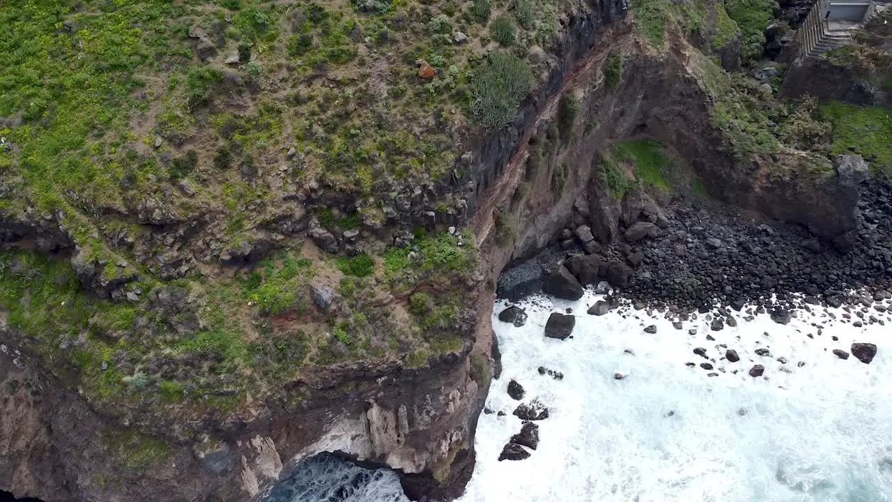 Top-down birdseye aerial drone view of dramatic cliffs dropping into the stormy ocean