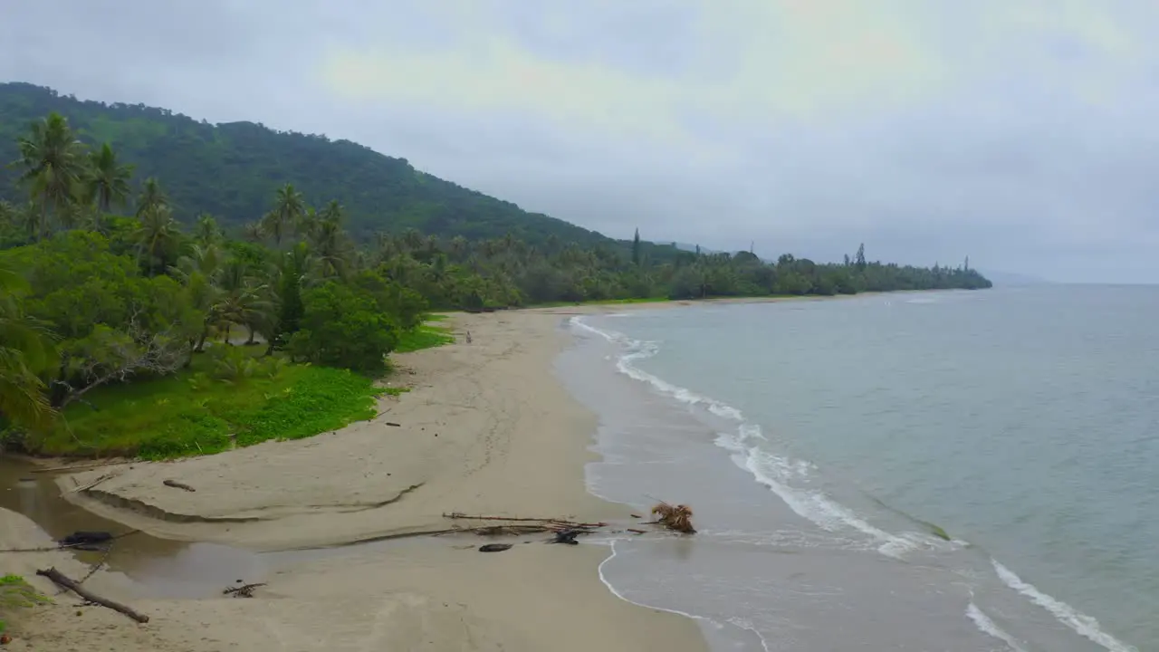 Drone traveling forward capturing the stormy beauty of a deserted tropical shoreline during a rainy day