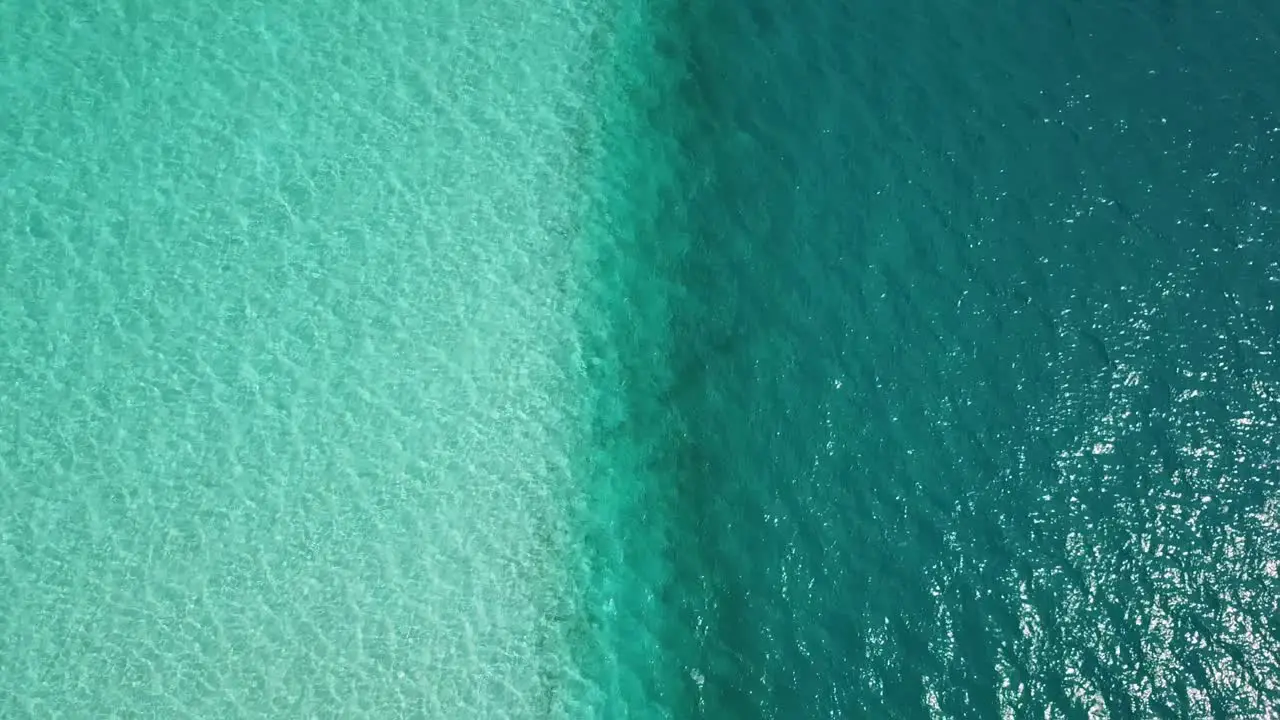 Aerial top down drone shot over turquoise aqua menthe ocean overlooking a line between shallow lagoon water and deeper teal colored sea on a sunny day in Maldives