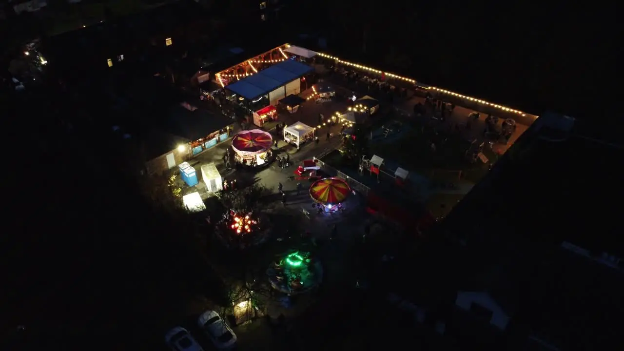 Illuminated Christmas funfair festival in neighbourhood pub car park at night aerial view