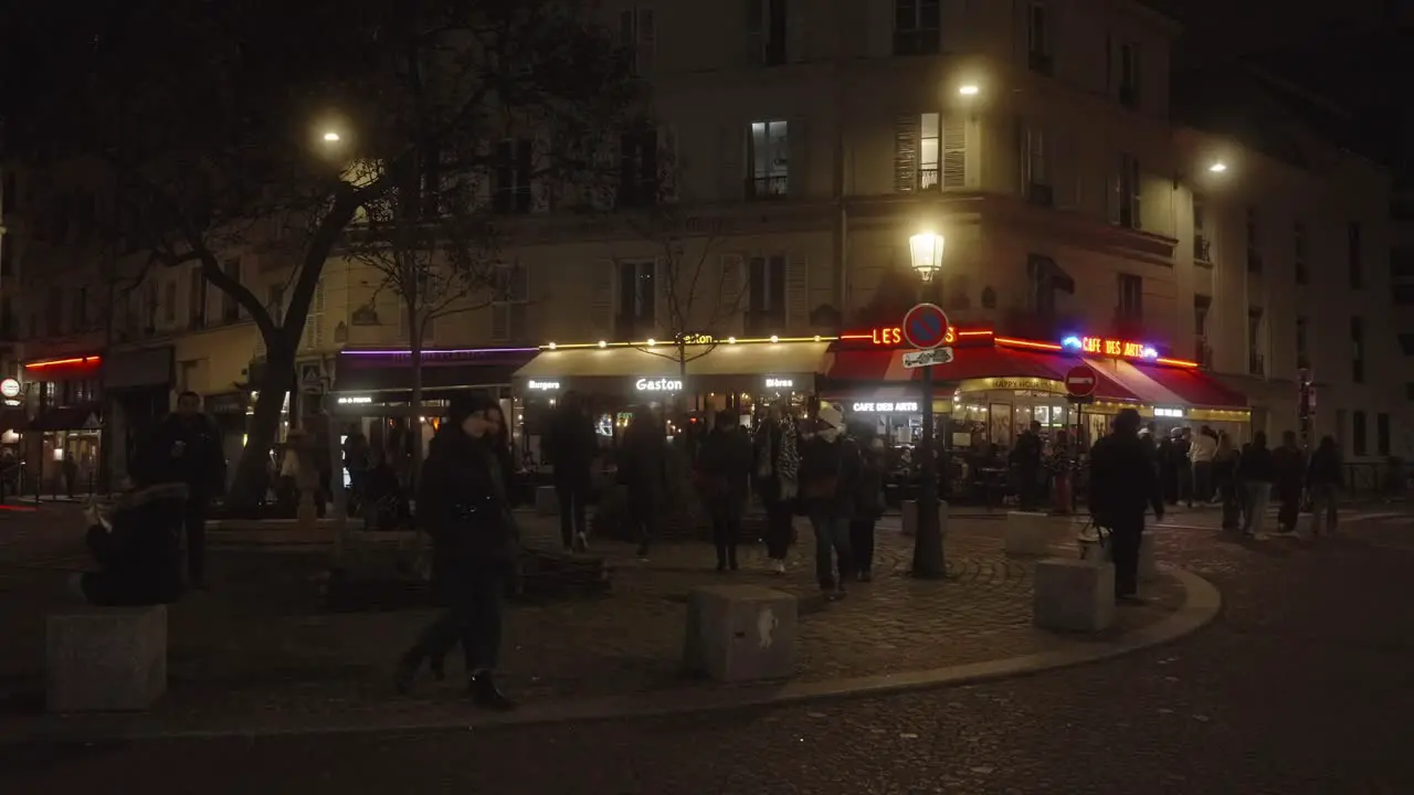 People walking over square in Paris during night time street lights and restaurants illuminate the street