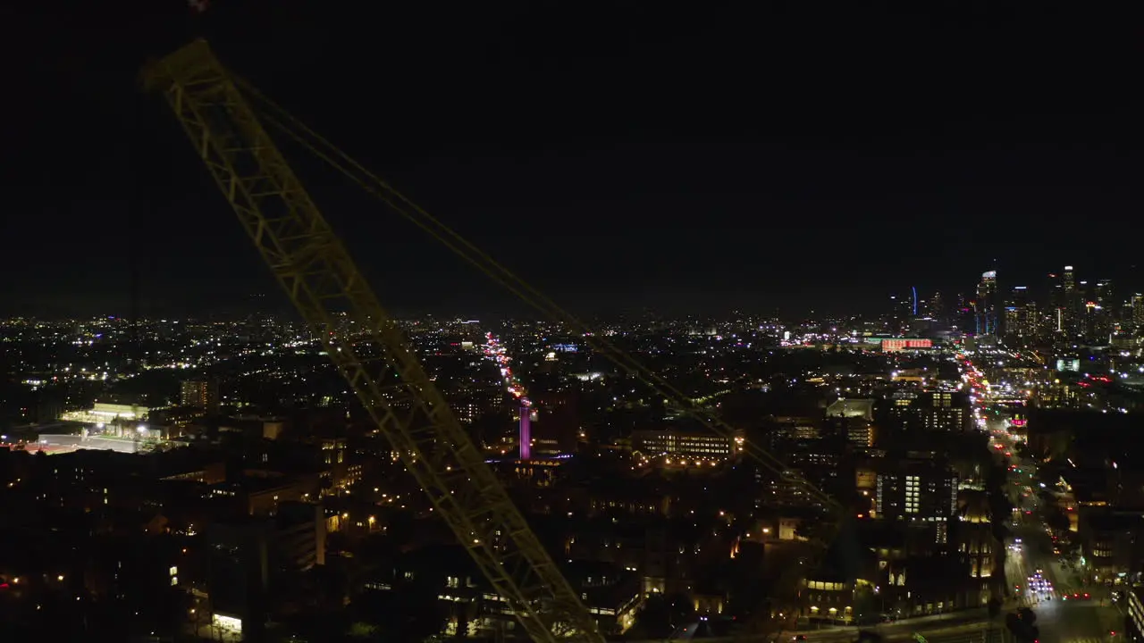 Aerial tracking shot of a construction crane with night lit LA cityscape background