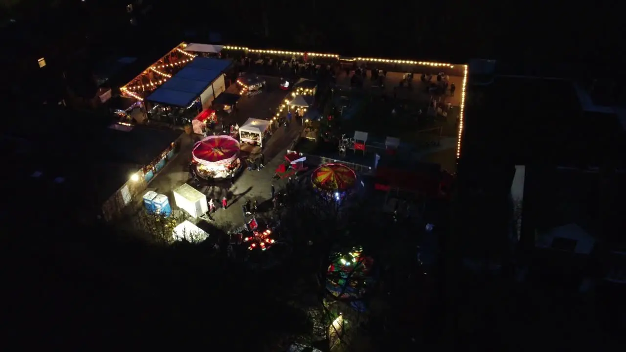 Bright Illuminated Christmas fairground festival in neighbourhood car park at night aerial view