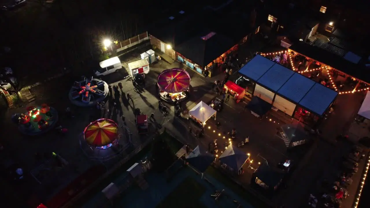 Illuminated Christmas fairground carnival in neighbourhood pub car park at night aerial view