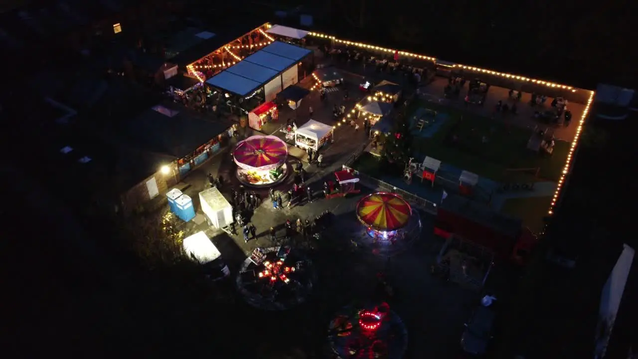 Illuminated Christmas spinning fairground rides in neighbourhood car park at night aerial view