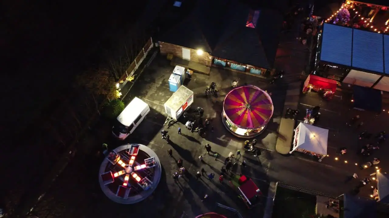 Illuminated Christmas spinning fairground rides in neighbourhood pub car park at night aerial view