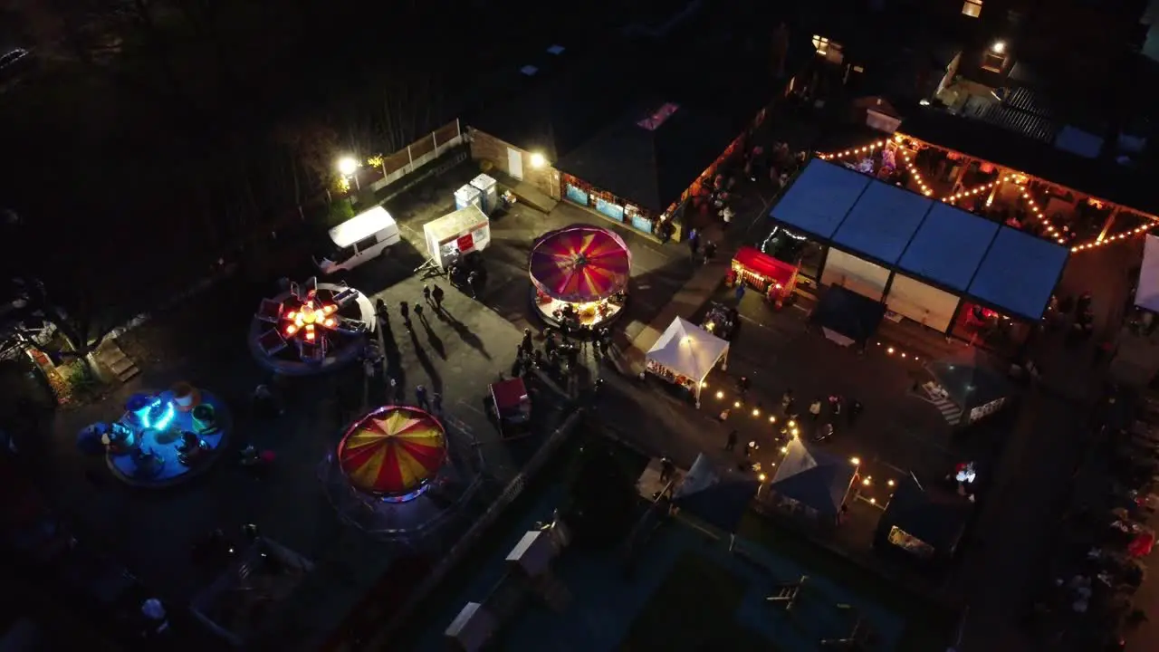 Illuminated Christmas amusement park in neighbourhood pub car park at night aerial view