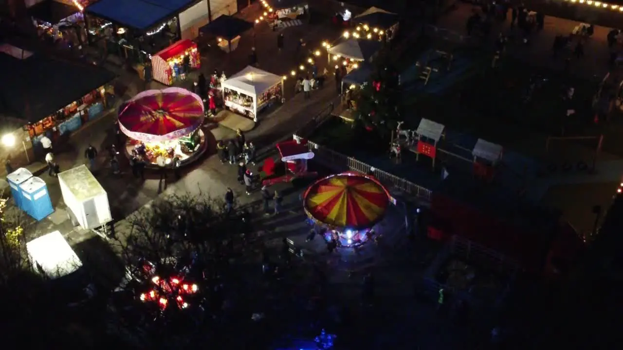 Illuminated Christmas fairground event in neighbourhood pub car park at night aerial view