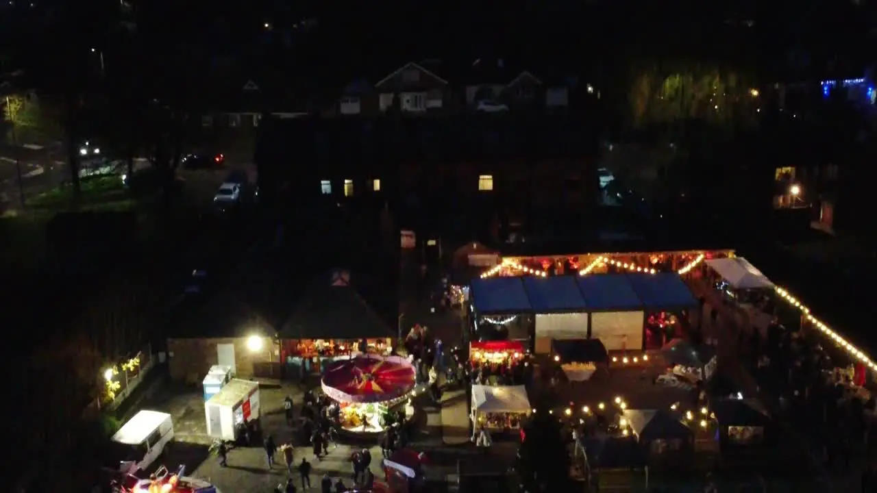 Illuminated Christmas funfair in neighbourhood pub car park at night aerial reveal view