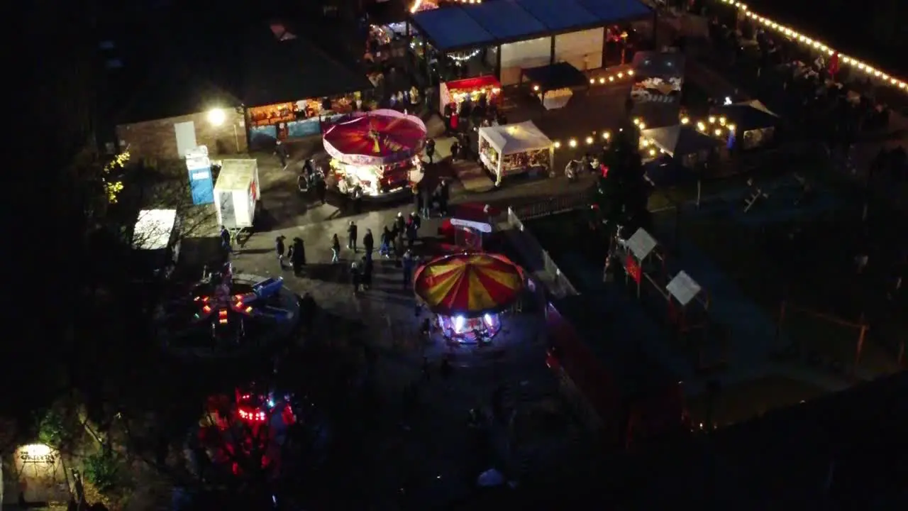 Illuminated Christmas fairground event in neighbourhood car park at night aerial view