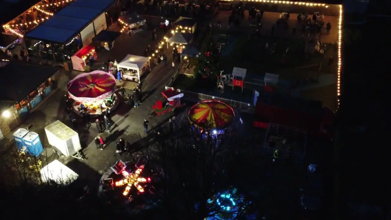 Illuminated Christmas fairground festivities in neighbourhood pub car park at night aerial view