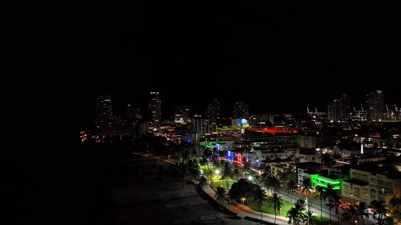 Beautiful nightly aerial drone footage of Miami USA rotating motion showing the coastline with palm trees and many different colored lights over the buildings