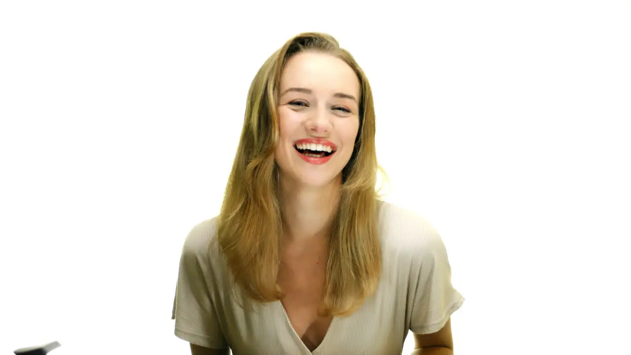 A close-up of a woman doing a full-body laugh and brushing her hair out of her face on a seamless white studio background