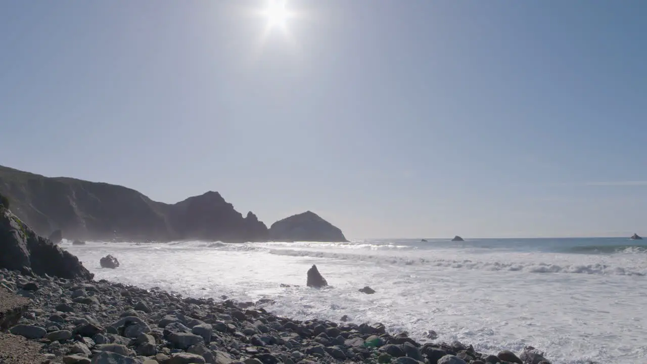 Low stationary shot of rolling waves crashing into the shore of Big Sur California Beach on a sunny day