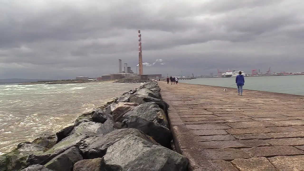 Some waves on the left and Dublin ESB Poolbeg in the centre with a shop on the right some people walking along the coast or south wall