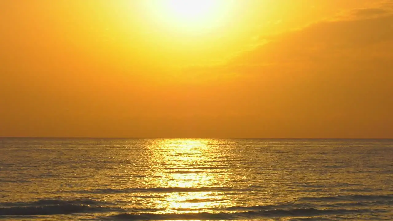 Golden sea reflecting sun rising in orange sky