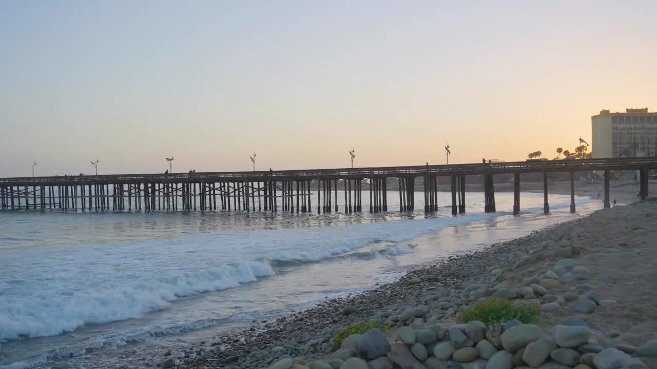 Panning shot of waves of the Pacific Ocean crashing along the shores of Ventura Pier as the sun sets located in Southern California