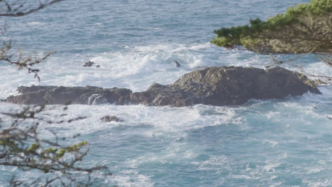 Stationary shot of Pacific ocean waters crashing against rocks on a sunny day located at Big Sur California