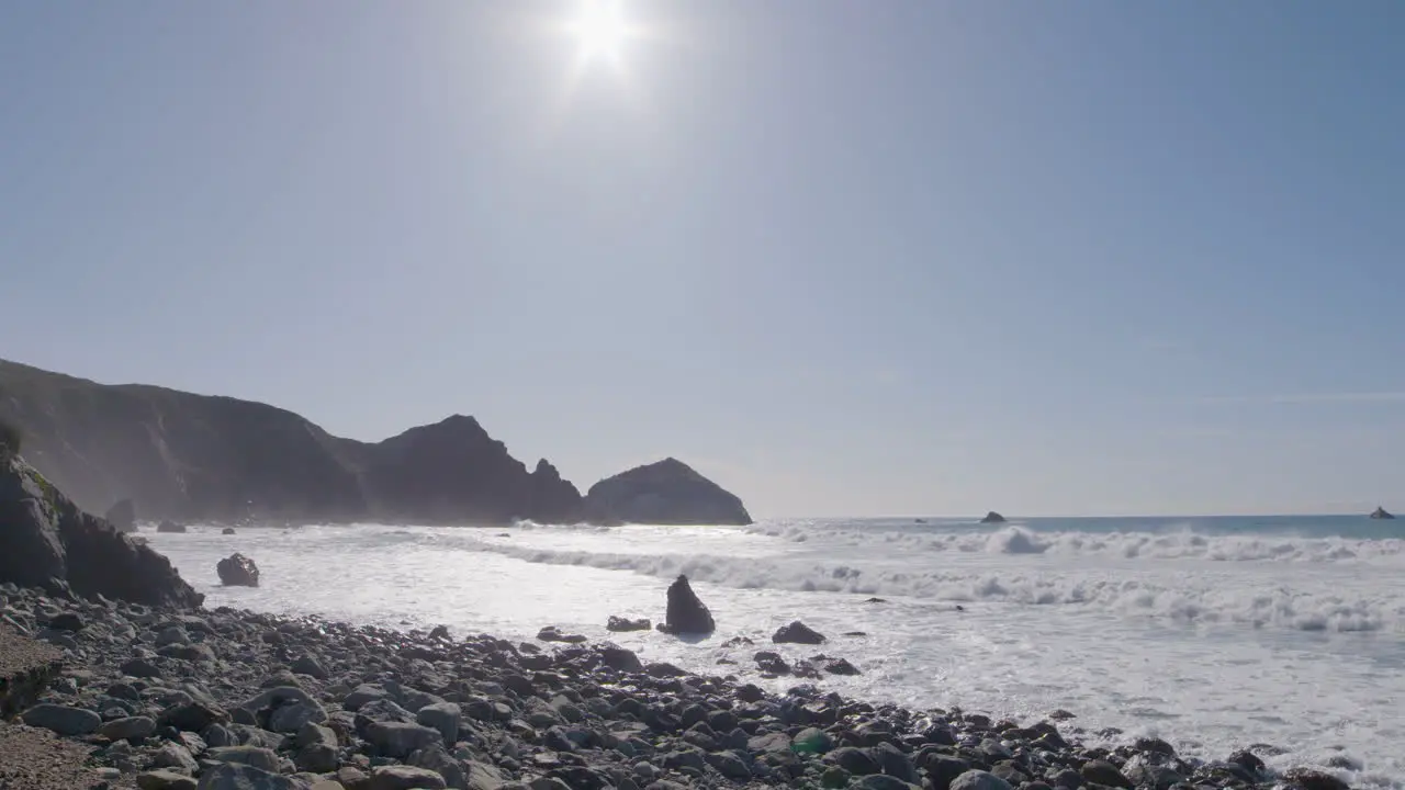 Low stationary shot of waves crashing along the rocky shores of Big Sur California Beach on a sunny summer day