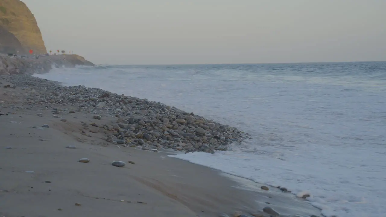 Panning shot from Pacific coast highway to the Pacific ocean as waves crash onto the shore at Mondo's Beach at dusk located in southern California