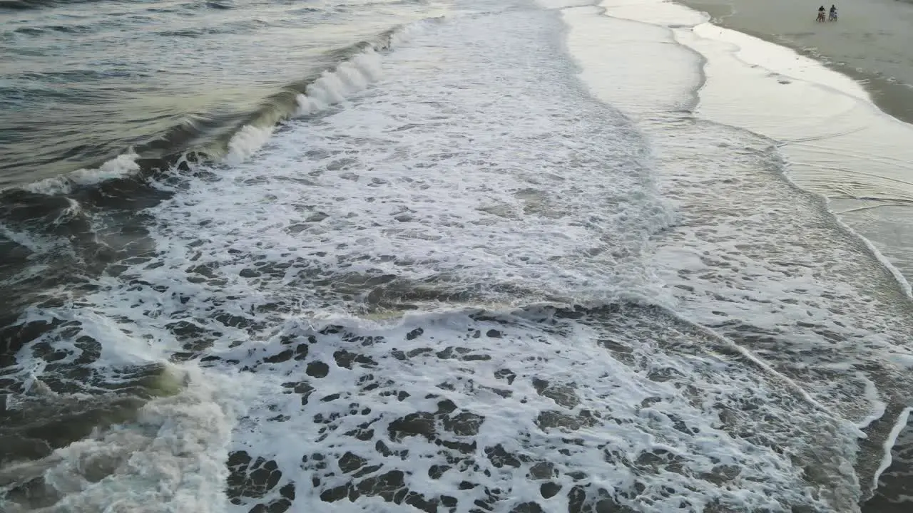 Wide drone shot flying down on beach with distant bicyclist